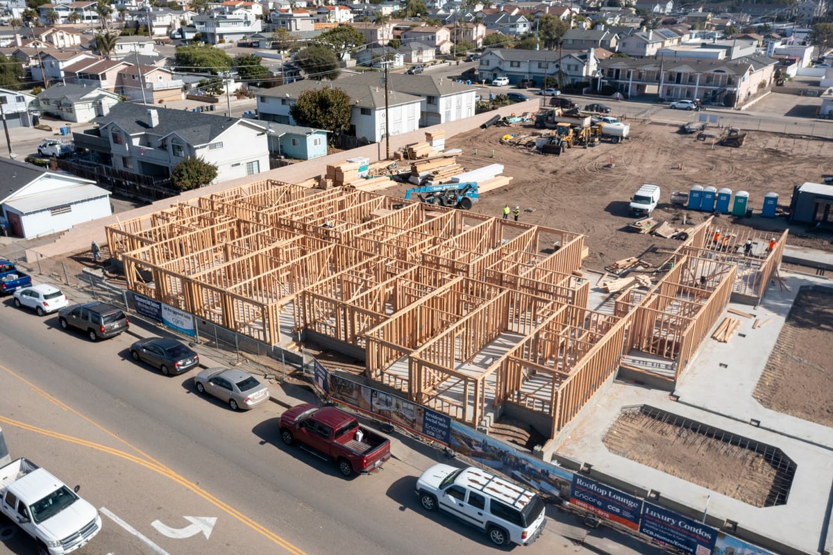 Aerial shot of Encore construction in Grover Beach, featuring the wooden framework of a multistory building in early stages, surrounded by construction equipment and materials, with residential neighborhoods and streets nearby, underlining the urban integration of this new development.